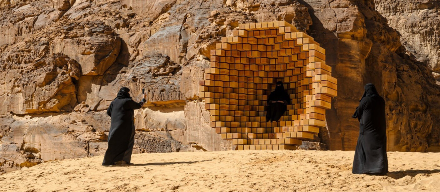 Skulptur zwischen Felsen in der Wüste, davon Fraeun in Burkas